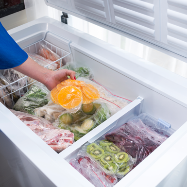 a women leans into a chest freezer, taking out fruit
